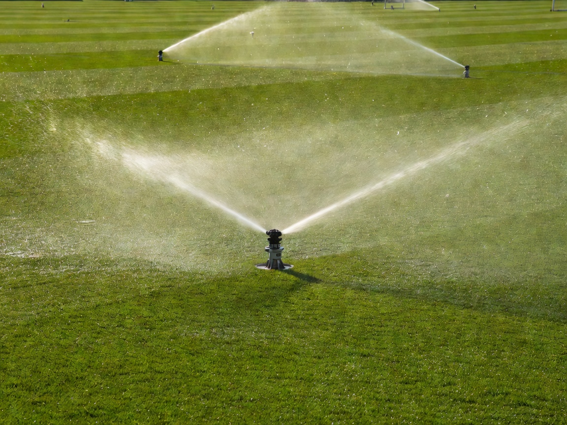 Technical pop-up sprinkler spraying fine water mist across football pitch turf